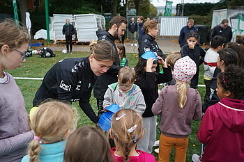 Juliane Wirtz (Spielerin des SV Werder Bremen) verteilt an Kinder kleine Hütchen zum Fußball spielen.