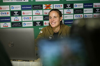 Hanna Németh lächelt während der Mixed Zone vor einem Laptop. Sie sitzt vor einer Sponsorenwand